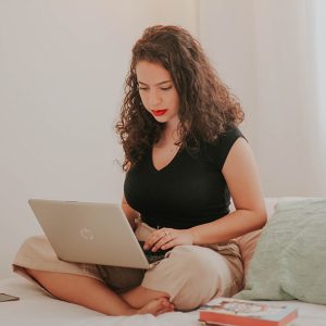 person sitting on bed cross-legged working on laptop