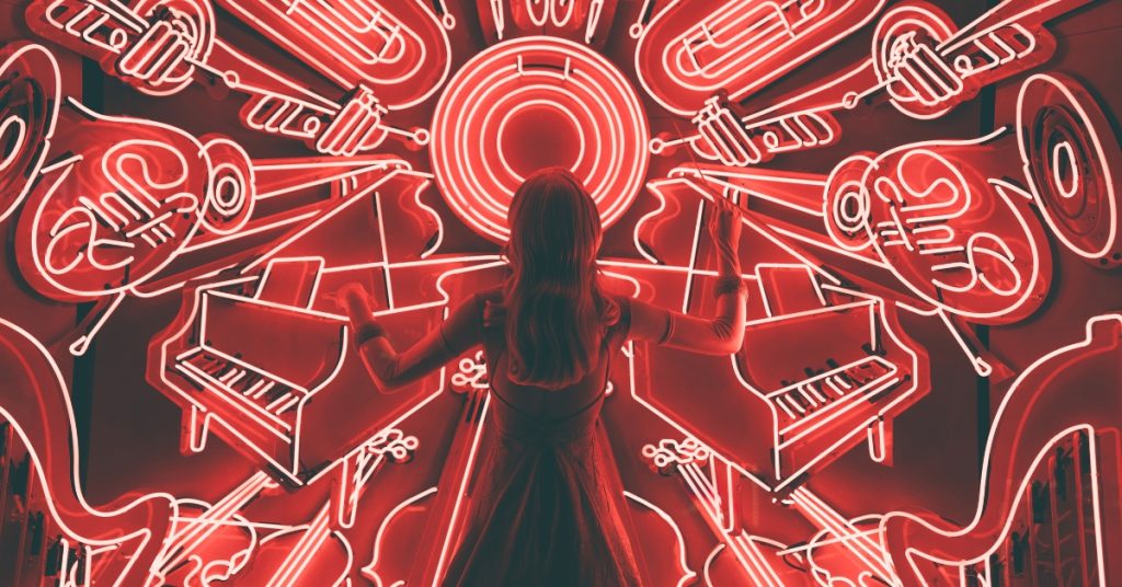 Person in dress standing with their back to camera, conducting a chaotic pattern of red neon instruments.