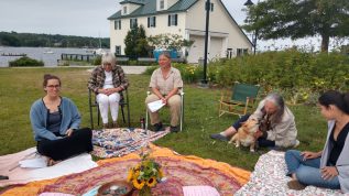 Five people sitting in circle around colorful tablecloth in the park by the bay in Belfast, Maine on a sunny day